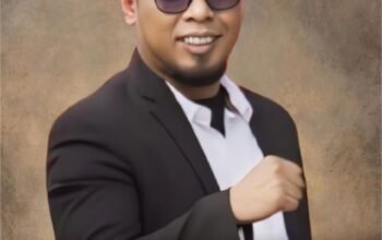 Abah Elang Mangkubumi mengenakan jas hitam dan peci khas Pagar Nusa, berpose dengan tangan mengepal sebagai simbol ketegasan dalam menolak proyek yang mengancam rakyat pesisir Serang.