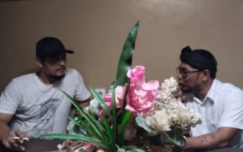 Dua tokoh sedang berdiskusi serius di sebuah meja dengan hiasan bunga di tengahnya; suasana hangat memperlihatkan perbincangan antara aktivis dan tokoh spiritual di Lebak.