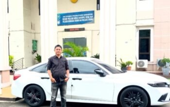 Ketua LBH, Andi Ambrillah,berdiri di depan mobil sedan putih yang terparkir di halaman sebuah gedung pemerintahan.