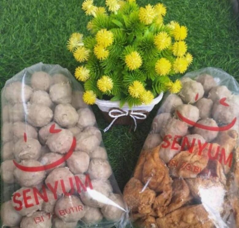 Kemasan bakso dan produk olahan daging merek Senyum dalam plastik bening dengan latar rumput sintetis